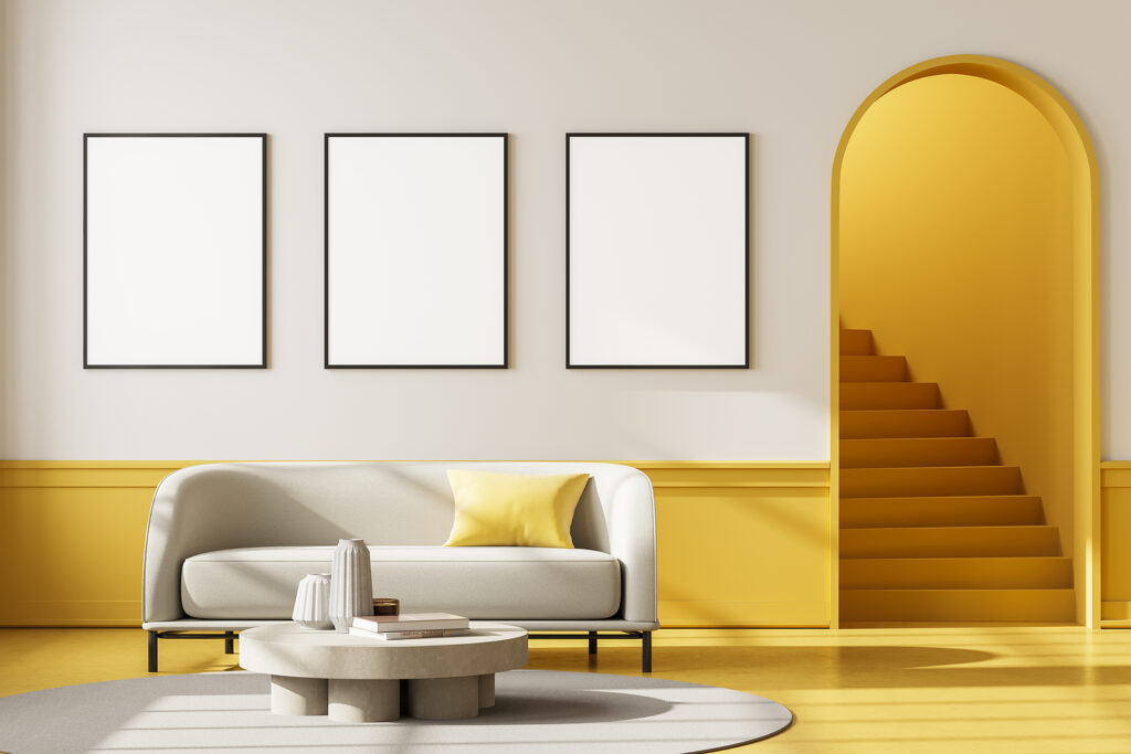 Apartment interior with white couch and coffee table on carpet with yellow floor. Mockup blank wall copy space with three posters, staircase with arch door