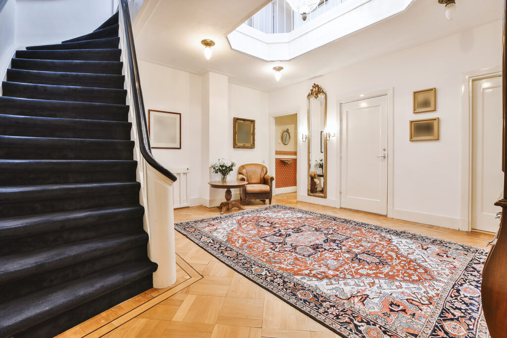 Ornamental carpet placed on floor near stairway in vintage hallway of elegant house