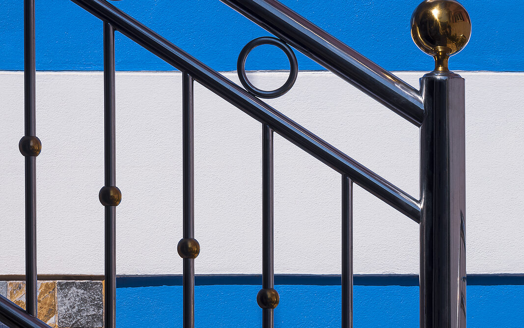Sunlight and shadow on surface of stainless steel handrail on outdoor staircase with blue and white wall decoration in vertical frame
