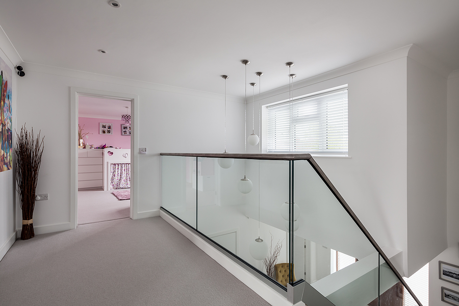 First floor landing in modern home with stainless steel and glass balustrade, white walls and door open to pink bedroom